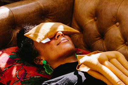 Woman lying on a couch with a yellow eye pillow resting on her eyes.